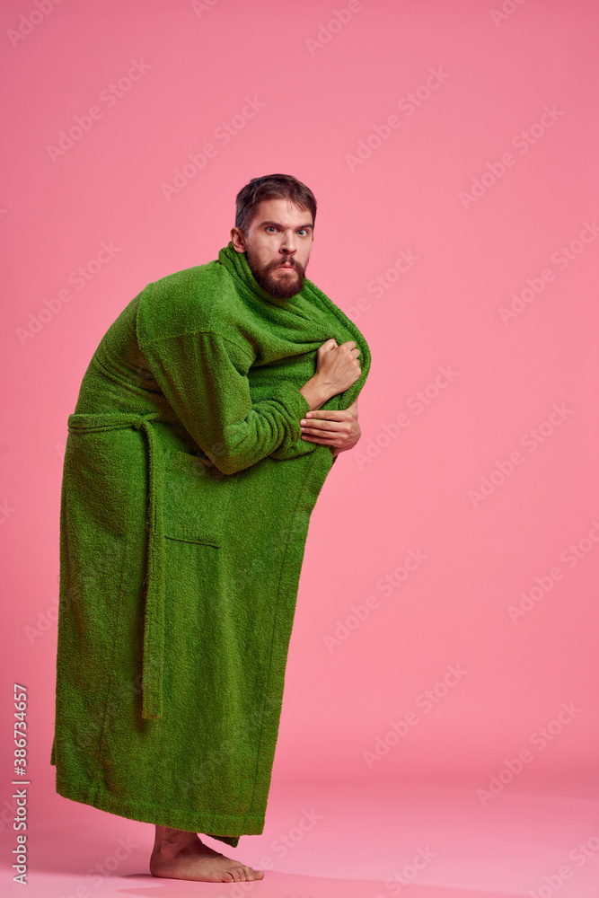 Fototapeta premium An emotional man in a green robe in full growth on a pink background gestures with his hands to the model