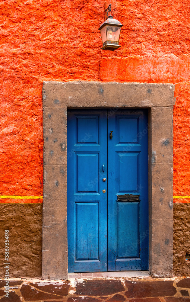 Fototapeta premium An old blue painted door with a fish knocker, stone frame and bright rough orange wall