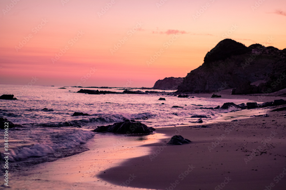 Beautiful sunset on a pristine beach with rocks in the background
