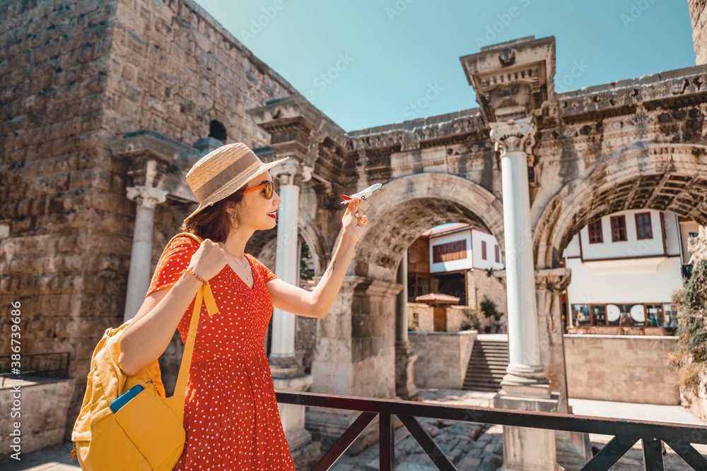 traveler with a toy plane on the background of the archaeological monument - the gate of the Emperor Hadrian in the old city of Antalya. Concept of air tickets and airlines in Turkey - obrazy, fototapety, plakaty 