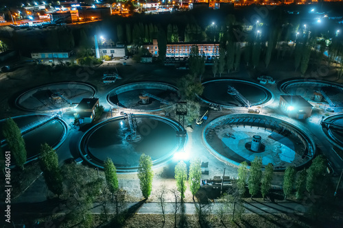 Wastewater Treatment Plant with tanks for purification and filtration of urban waste water, aerial view at night.