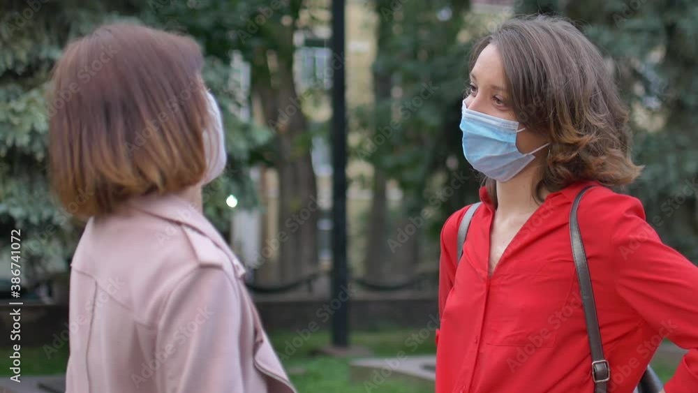 Happy meeting of two female friends wearing face mask and keep social distance at the street on trees background, friendship and communication during quarantine Happy meeting of two female friends wearing face mask and keep social distance at the street on trees background, friendship and communication during quarantine