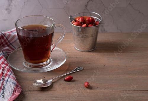 A Cup of vitamin tea with rosehip and a tin bucket of fruit on a brown wooden background . Natural herbal tea. Horizontal orientation photo