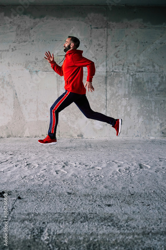 Side view of fit runner in tracksuit running fast in urban exterior.