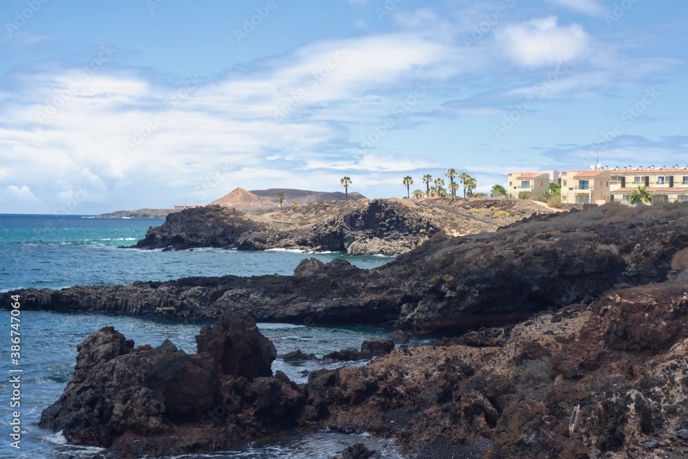 The black lava coast on the south coast of the Canary island of Tenerife. In the background is a small settlement in the village of 