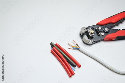 wire stripper, shielded three-core wire and heat shrink tubing on a white background. close-up photo