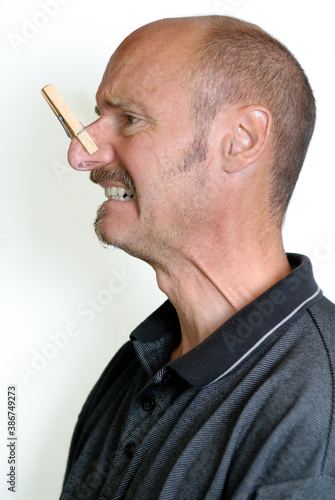 Profile of grimacing man with a clothes pin on large nose