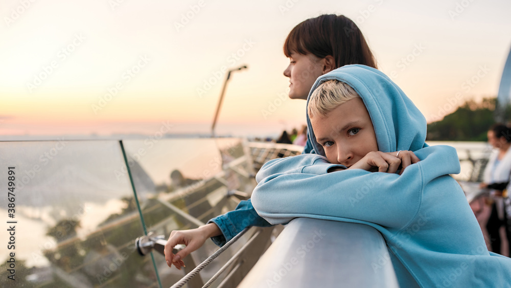 Young lesbian woman looking at camera while enjoying romantic moments together with her girlfriend, standing on the bridge, admiring sunrise