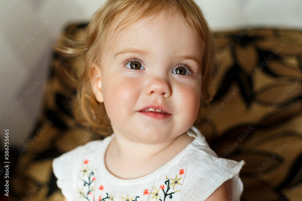 A 2 years old girl is sitting on the bed and smiling. The child rejoices and turns over. Happy child A 2 years old girl is sitting on the bed and smiling. The child rejoices and turns over. Happy child