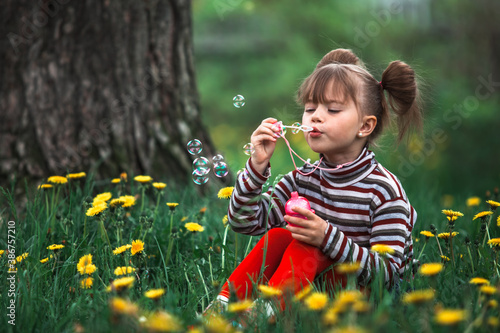 Little cute girl blowing soap bubbles in the park.