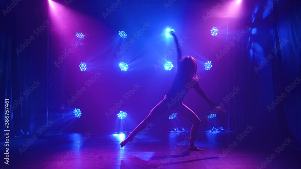 Sexy modern contemporary dance contempt performed by a flexible young woman. The dancer is enjoying the dance and hovering in a dark studio with neon lights. Silhouette. Slow motion. Sexy modern contemporary dance contempt performed by a flexible young woman. The dancer is enjoying the dance and hovering in a dark studio with neon lights. Silhouette. Slow motion.