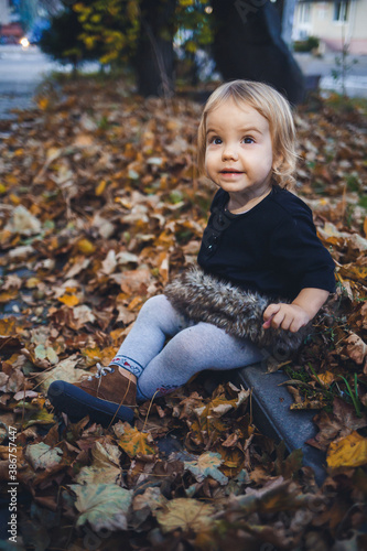 A little girl of 1.5 years is standing and smiling. The child throws leaves. Cheerful girl in the autumn forest