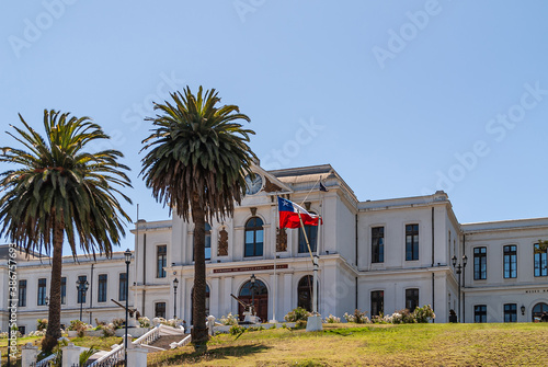 Valparaiso, Chile - December 8, 2008: White historic building of Navy Headquarters on green lawn hill under blue sky with couple of palm trees and a few machine guns. Flag adds color. © Klodien