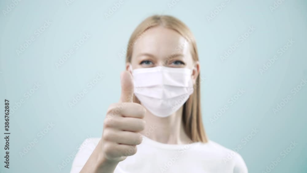 Happy woman in medical mask look and show thumb up, cool, to the camera on light background. Health protection Corona Virus concept, Covid-19 pandemic. Health care, selective focus, 4k Happy woman in medical mask look and show thumb up, cool, to the camera on light background. Health protection Corona Virus concept, Covid-19 pandemic. Health care, selective focus, 4k