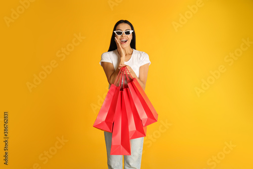 Beautiful young woman with paper shopping bags on yellow background