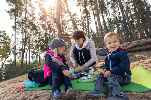 Young adult caucasian beautiful mother enjoy having fun eating snack on picnic with two cute little children in pine forest outdoors on warm autumn day. Family nature outdoor recreation lifestyle © Kirill Gorlov