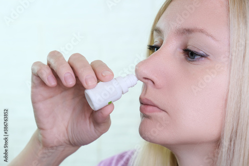 A woman with a runny nose holds a medicine in her hand, nasal spray irrigations to stop allergic rhinitis and sinusitis