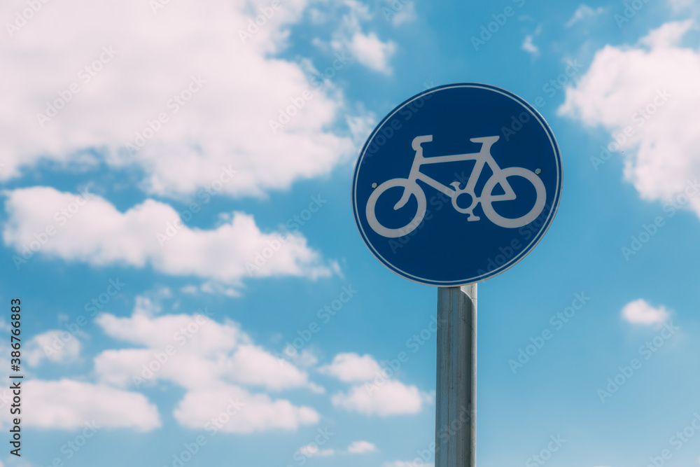 Close-up view of round blue and white bicycle lane sign against a blue sky with clouds. Outdoor sign. Traffic Laws. One circle road sign on a pillar. Street signs. Safe bike ride.