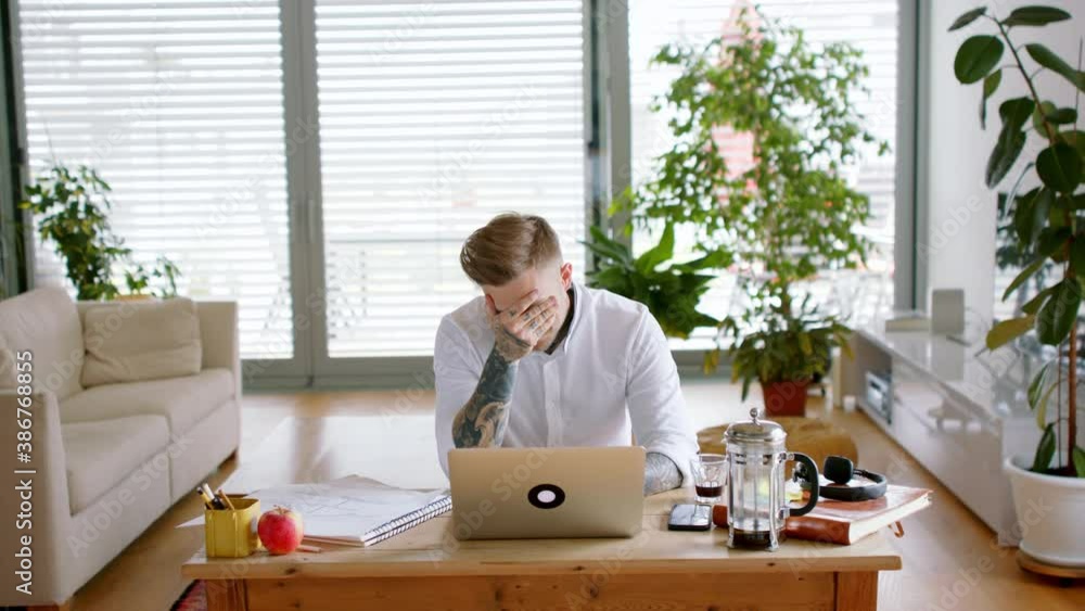 Disappointed young architect working with laptop indoors in home office, bad news concept. Disappointed young architect working with laptop indoors in home office, bad news concept.