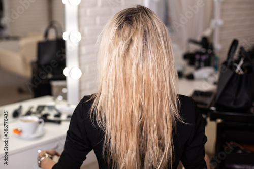 Female back with long blonde damaged hair in hairdressing salon