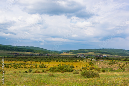 Summer mountain landscape. A village and a road against the background of mountains in the Cis-Baikal basin. Irkutsk region, Russia