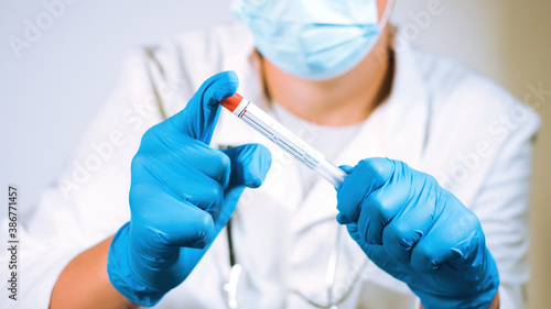 Doctor holding coronavirus swab test sample in a vial with gloves and face mask at laboratory. Close up