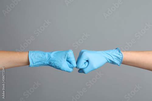 Doctors in medical gloves making fist bump on grey background, closeup