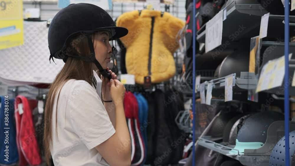 Young woman is buying a riding helmet in sports store Young woman is buying a riding helmet in sports store
