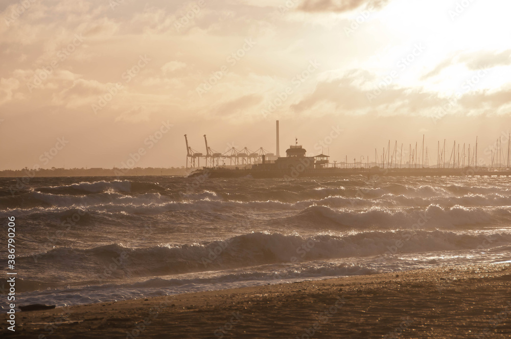 MELBOURNE, AUSTRALIA - JULY 29, 2018: Dramatic golden light ray from the sky in the afternoon with St Kilda pier and windy ocean in Melbourne bay and high tide wave. Nobody is in the photo.