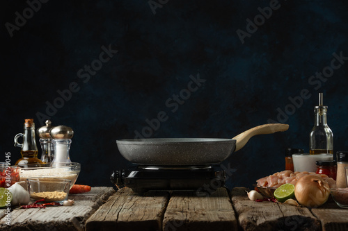 Wok pan on electric stove at rustic wooden table with ingredients background. Concept of coking meal.