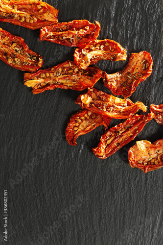 Red sun dried tomatoes with sunlight and shadow on black background. Tasty small slices tomato with spices and olive oil.