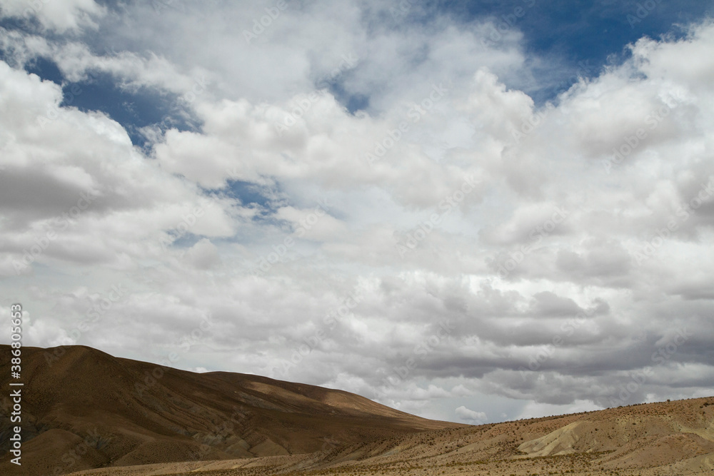 Naklejka premium Desert landscape. View of the arid hills and brown valley under a beautiful summer sky with white clouds.