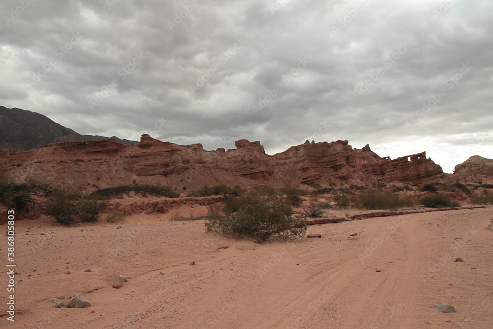 Red canyon. View of the arid desert, red sand, shrubs bushes, sandstone and rocky formation under a cloudy sky.