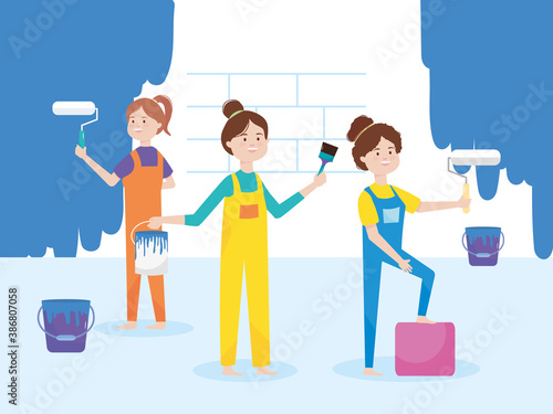 young women in overalls paint the wall with rollers brush and buckets remodeling