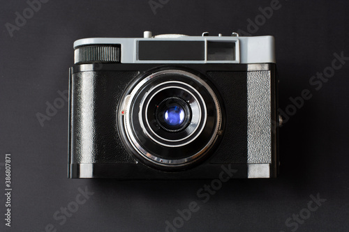 Retro film photo camera with blue lens reflection on black background. Top view. Close up
