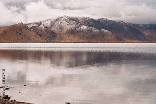 Snow mountain with reflection on lake and cloudy sky in brown tune.