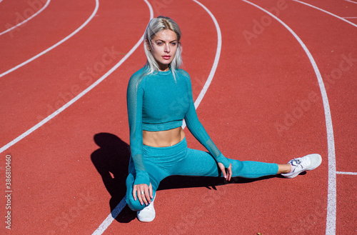 sexual athletic woman in fitness costume stretching on running track, sport