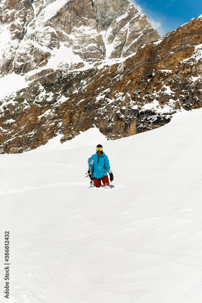 Full length image of a snowboarding standing in a snow, high mountain background.