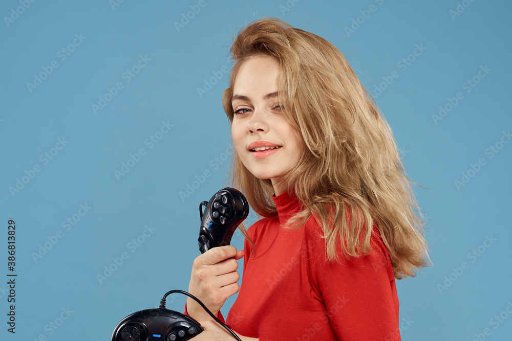 Fototapeta premium Woman holding in her hands two game controllers entertainment lifestyle red jacket blue background