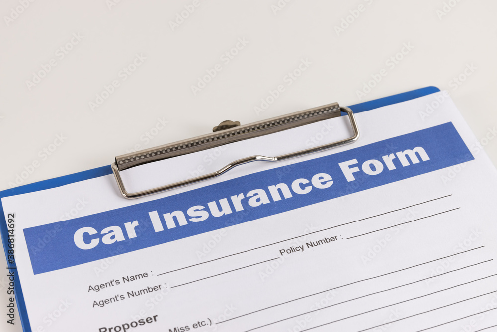 Car Insurance Claim Form or Auto Insurance Document on Left Slant and Clipboard on White Office Table