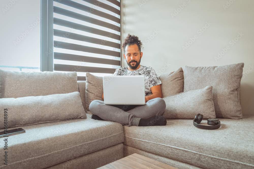 joven mexicano trabajando desde casa en sofa con computadora personal comodo joven mexicano trabajando desde casa en sofa con computadora personal comodo