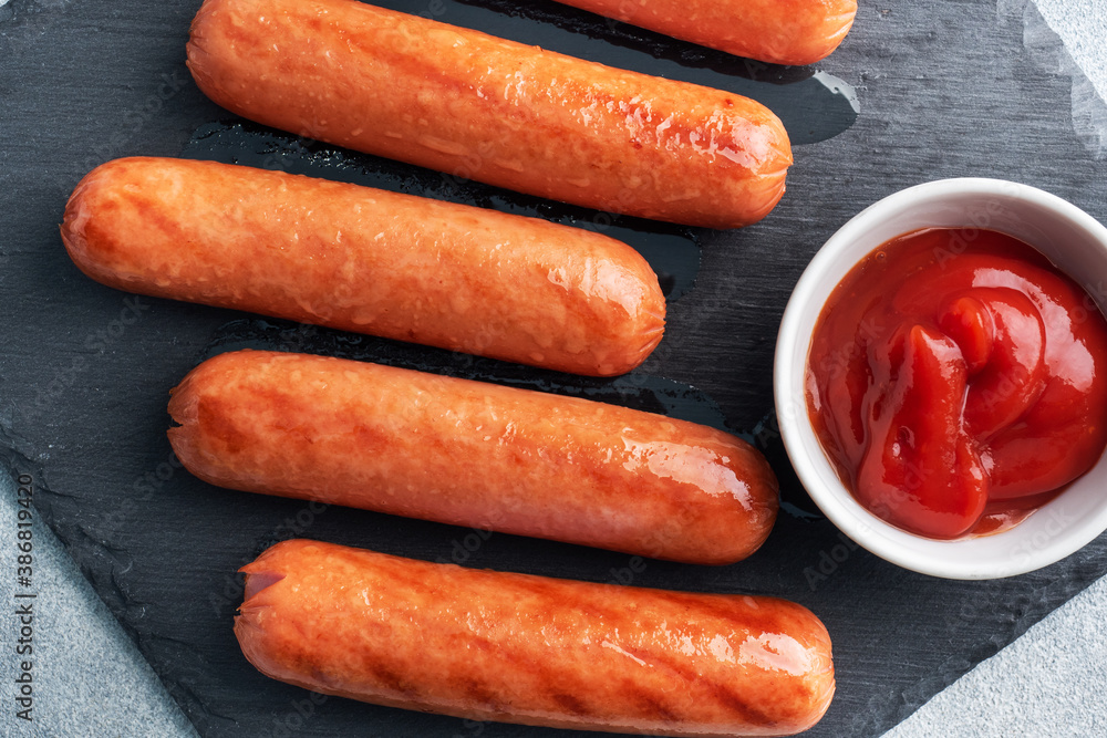 Juicy grilled meat sausages with tomato sauce and ketchup on a concrete stand. Fat fast food. Concept unhealthy eating. Juicy grilled meat sausages with tomato sauce and ketchup on a concrete stand. Fat fast food. Concept unhealthy eating.