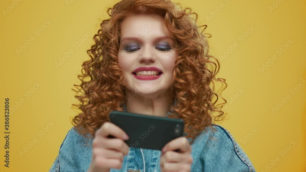 Woman playing game on smartphone at yellow background. Stylish girl using phone Woman playing game on smartphone at yellow background. Stylish girl using phone