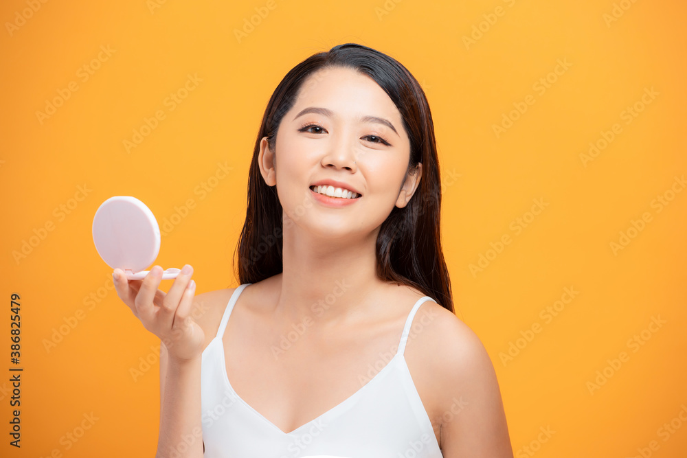 Beauty portrait of a smiling woman holding mirror isolated on a yellow background Beauty portrait of a smiling woman holding mirror isolated on a yellow background