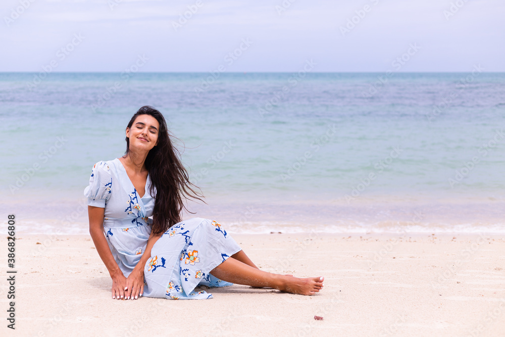 Romantic portrait of woman in long blue dress on beach by sea at windy day.  