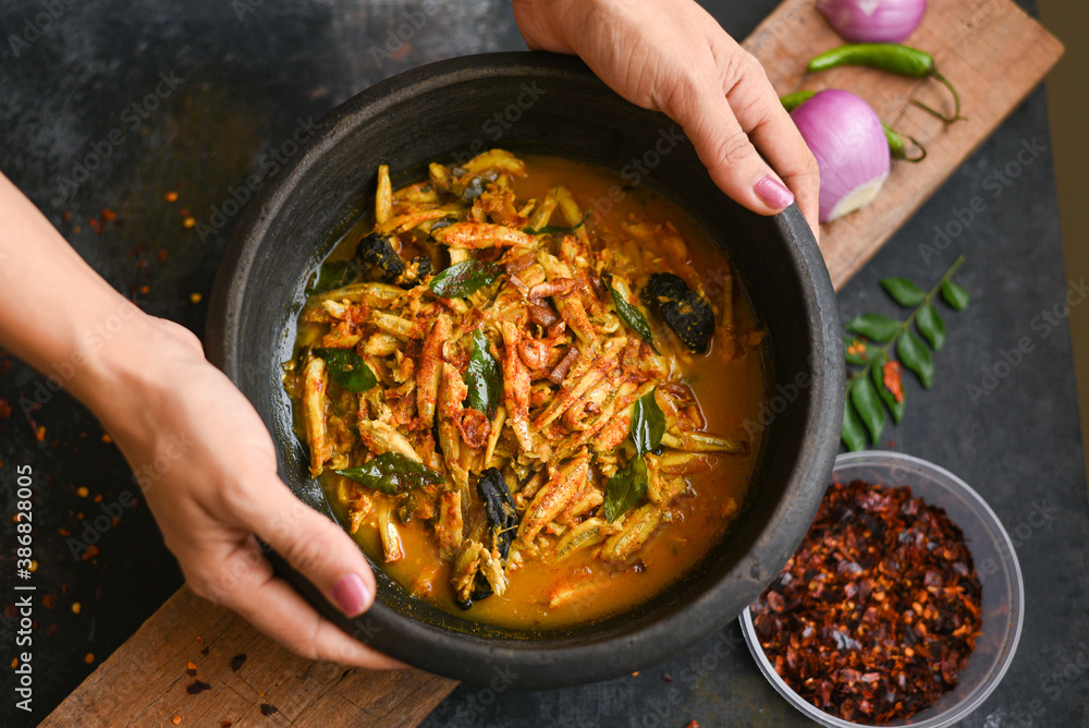 Top view spicy hot anchovy Kerala fish curry. Indian food. Woman hand making Fish curry with red