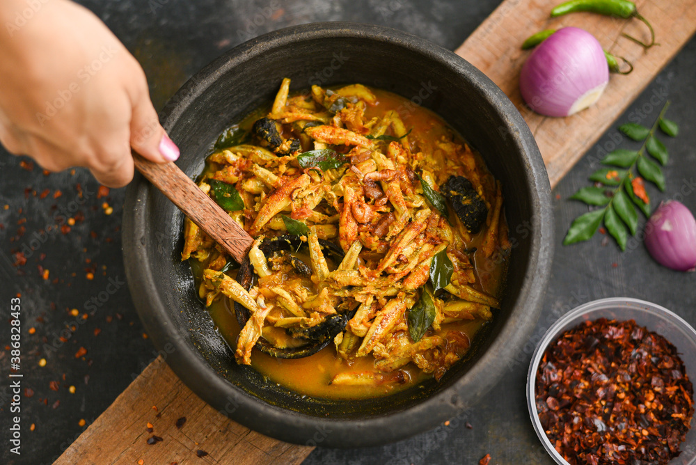 Top view spicy hot anchovy Kerala fish curry. Indian food. Woman hand making Fish curry with red