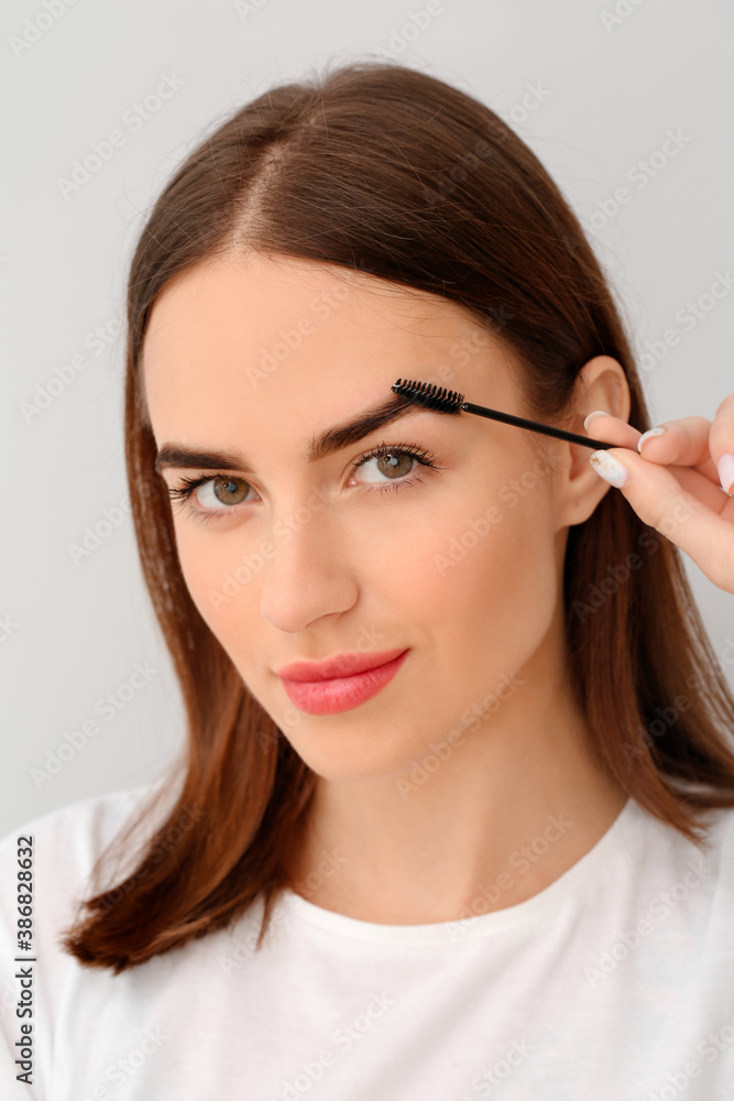 Young woman undergoing eyebrow correction procedure on light background