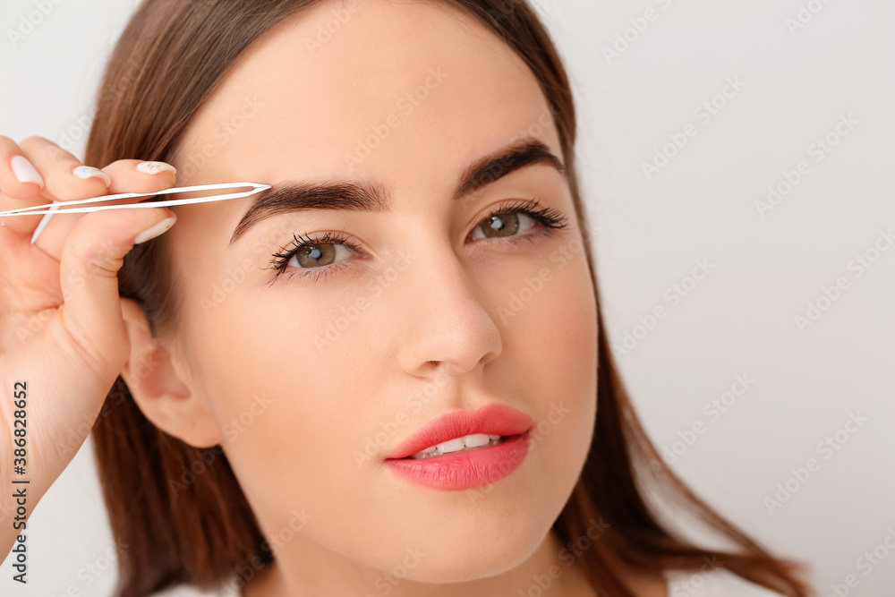 Young woman undergoing eyebrow correction procedure on light background