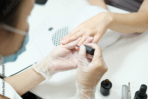 manicurist applying moisturising oil on finger nails for anti age nail care. rejuvenating and fortifying treatment in beauty salon. beautyful hands. professional care.